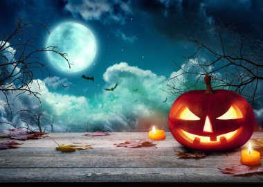 Ürkütücü Cadılar Bayramı balkabakları, Jack O 'Lantern, şeytani bir yüzü ve gözleri olan, sisli bir arka planı ve dolunayı olan tahta bir masa. Kara sisli arka planı olan Cadılar Bayramı Balkabağı.