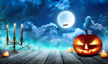 Ürkütücü Cadılar Bayramı balkabakları, Jack O 'Lantern, şeytani bir yüzü ve gözleri olan, sisli bir arka planı ve dolunayı olan tahta bir masa. Kara sisli arka planı olan Cadılar Bayramı Balkabağı.