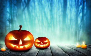 Ürkütücü Cadılar Bayramı balkabakları, Jack O Fenerleri. Ahşap bir masada, sisli, gri bir arka planı olan şeytani bir yüzü ve gözleri var. Karanlık bir geçmişi olan Cadılar Bayramı Balkabağı.