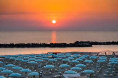 Güneşin doğuşuyla güzel bir gün doğumu, Rimini sahilinde şemsiyeli.