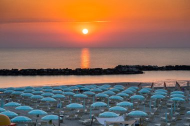 Güneşin doğuşuyla güzel bir gün doğumu, Rimini sahilinde şemsiyeli.