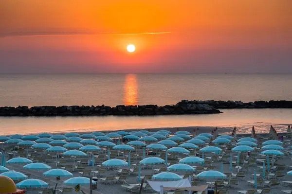 stock image Beautiful sunrise with sun reflection on Rimini beach with umbrellas