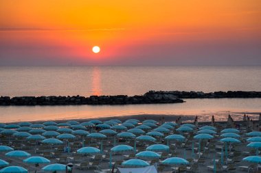 Beautiful sunrise with sun reflection on Rimini beach with umbrellas clipart