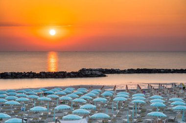 Güneşin doğuşuyla güzel bir gün doğumu, Rimini sahilinde şemsiyeli.