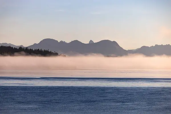 Спокойное Озеро Окутанное Туманом Величественными Горами Заднем Плане Создавая Потрясающий Стоковое Фото