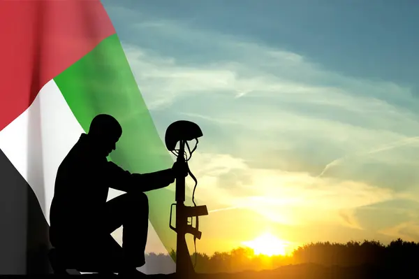 Silhouette of a solider kneeling down with UAE flag against the sunset. Concept - UAE national holidays, National Day, Commemoration Day