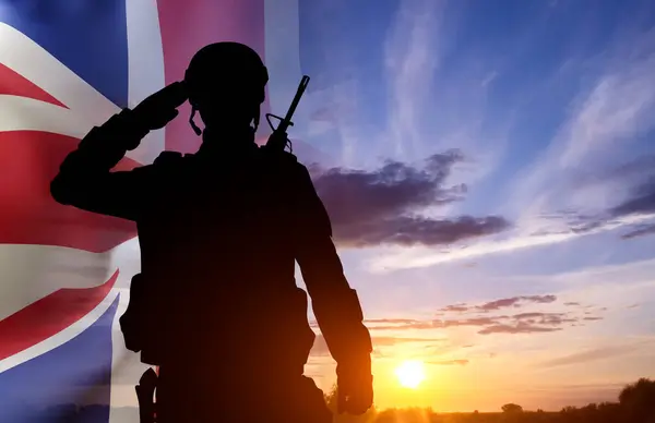 stock image Silhouette of a soldier with United Kingdom flag against the sunset. Background for Remembrance Day. United Kingdom Armed Forces concept