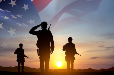 Gün batımına karşı Amerikan bayrağı taşıyan bir askerin siluetleri. Anma Günü, Gaziler Günü