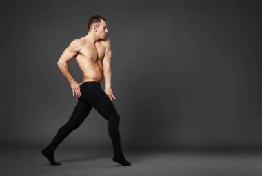 Full body portrait of a young ballet dancer dancing against a gray background.