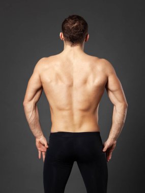 Full-length portrait of a young ballet dancer photographed from behind, standing in front of a gray background.
