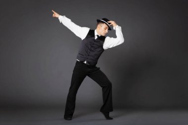 Confident young man dancing in gangster style suite. Studio shot isolated on gray background.