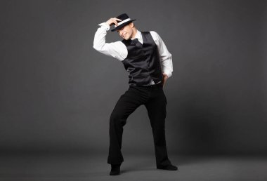 Confident young man dancing in gangster style suite. Studio shot isolated on gray background.
