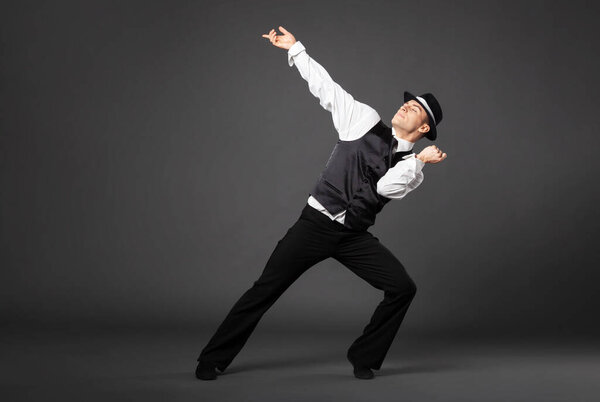 Confident young man dancing in gangster style suite. Studio shot isolated on gray background.