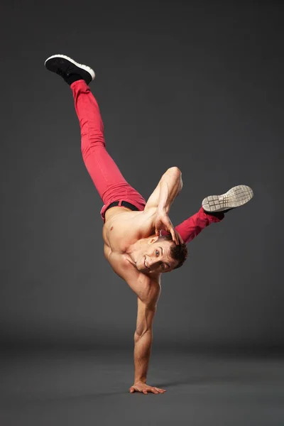 Young male professional dancer B-boying in studio isolated on gray background.