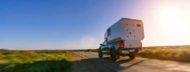 expedition camping van pick up truck on a dirt road on a sunny afternoon.