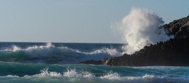 huge beautiful wave is breaking at the coastline while a breeze blows the spit water out of the sea at a wonderful sunset with orange sky