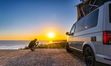 man sitting with digital device at his Transporter Camping Van bus at the California Ocean in the coastal Nature - digital nomades concept