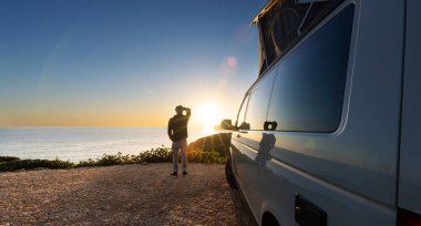man sitting with digital device at his Transporter Camping Van bus at the California Ocean in the coastal Nature - digital nomades concept