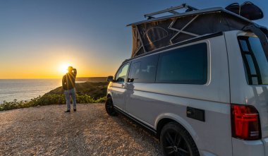 man sitting with digital device at his Transporter Camping Van bus at the California Ocean in the coastal Nature - digital nomades concept