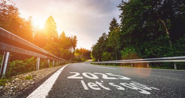 Yeni yıl 2025 ya da düz ve başlangıç konsepti. 2025 numara gün batımında yolda mercek parlamasıyla yazılmış. Zorluk kavramı veya kariyer yolu, iş stratejisi.