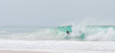 Genç yetişkin okyanusta büyük bir dalgada sörf yapıyor.
