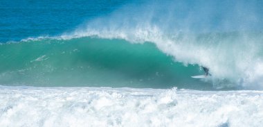 Genç yetişkin okyanusta büyük bir dalgada sörf yapıyor.