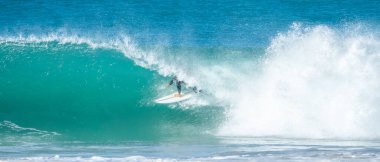 Genç yetişkin okyanusta büyük bir dalgada sörf yapıyor.
