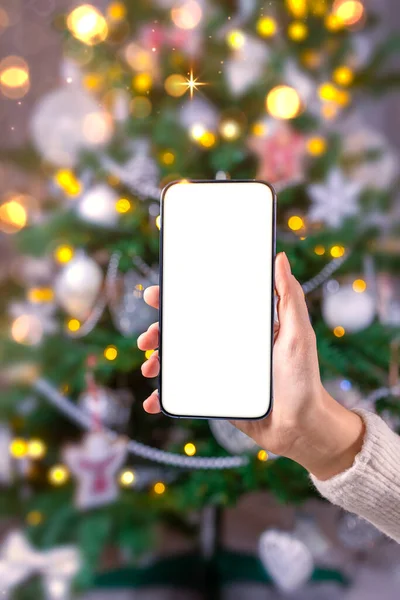クリスマスツリーで休日の背景に空の画面のモックアップとスマートフォンを閉じます 手に携帯電話を保持顧客 オンラインショッピング ギフトを購入 検索情報 閲覧アプリ — ストック写真