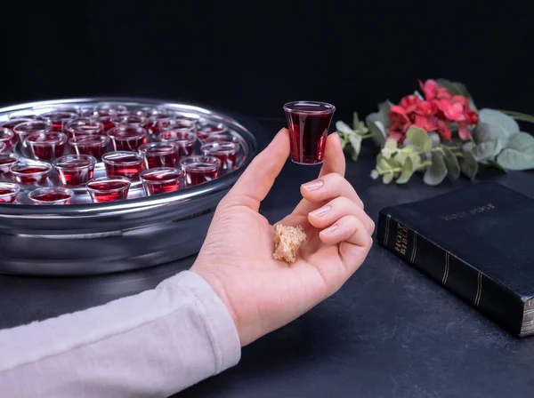 Closeup of young woman taking communion the wine symbol of Jesus Christ blood in small cups on black background. Easter Passover and Lord Supper concept.