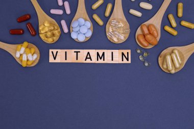 Ahşap kaşıklardaki farklı vitaminler ve gri arka planda yazılar. Haplar, uyuşturucular, ilaveler, ilaçlar, eczane ve sağlık hizmetleri kavramı.