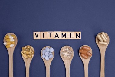 Ahşap kaşıklardaki farklı vitaminler ve gri arka planda yazılar. Haplar, uyuşturucular, ilaveler, ilaçlar, eczane ve sağlık hizmetleri kavramı.