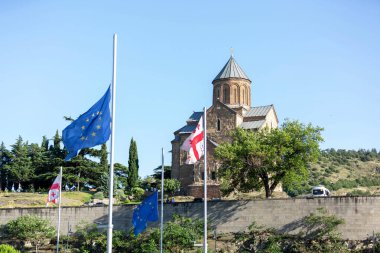 Tbilisi, GEO - June 22, 2024: Georgian and EU flags in front of the Metekhi church, located on the left bank of the river Kura, Tbilisi. clipart