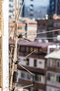 Şehir merkezinin duvarındaki eski televizyon ve radyo antenleri kapalı ve güneşli yaz gününde arka plandaki apartmanların açık penceresinden görülüyor.