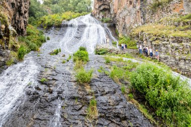 Jermuk, Ermenistan - 3 Ağustos 2024: Yağmurlu yaz günlerinde Arpa nehri vadisinde turistlerle Jermuk Şelalesi manzarası