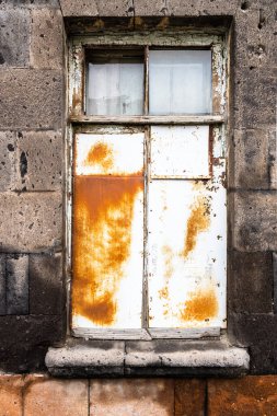 window in old house made of black tuff is covered with rusty tin in Gyumri city, Armrnia on overcast summer day clipart