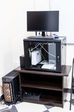 Ofis odasının köşesinde sunucu, yönlendirici, bilgisayar monitörü ve kesintisiz güç kaynağıyla ahşap duruş.