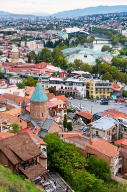 Tiflis, Gürcistan - 23 Eylül 2023: bulutlu bir sonbahar gününde Narikala kalesinden Aziz George Kilisesi ve Barış Köprüsü ile Tiflis şehri manzarası üzerinde