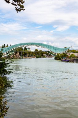 Tiflis, Gürcistan - 26 Eylül 2023: Bulutlu bir sonbahar gününde Tiflis şehrindeki Kura Nehri üzerinde modern Barış Köprüsü