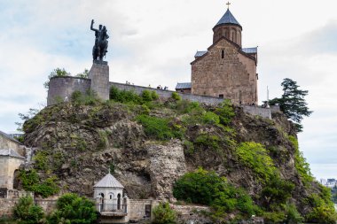 Tbilisi, Georgia - September 26, 2023: bottom view of equestrian statue of King Vakhtang Gorgasali and Virgin Mary Assumption Church of Metekhi in Tbilisi city on cloudy autumn day clipart