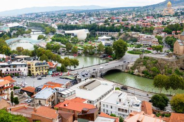 Tiflis, Gürcistan - 23 Eylül 2023: Bulutlu bir sonbahar gününde Narikala kalesinden Metechi köprüsü ile Tiflis şehri manzarası üzerinde