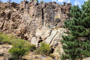 Goght, Ermenistan - 30 Eylül 2023: Güneşli sonbahar gününde Yukarı Azat Vadisi 'ndeki Geghard Manastırı' ndaki uçurumlarda mağaralar. Geghard UNESCO Dünya Mirası Listesi