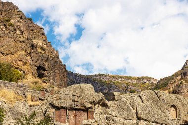 Goght, Ermenistan - 30 Eylül 2023: Güneşli bir sonbahar gününde Yukarı Azat Vadisi 'ndeki Geghard Manastırı' nda uçurumda haçkarlar ve mağaralar. Geghard UNESCO Dünya Mirası Listesi