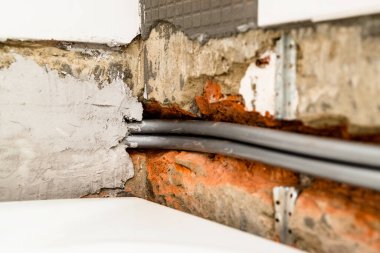 installation of new polyethylene flexible plumbing pipes in chiseled brick wall above white bathtub under removed ceramic tiles during installation of new water supply in bathroom clipart