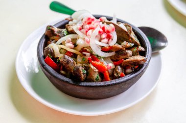 travel to Georgia - portion of Kuchmachi (Georgian dish of livers, hearts and gizzards with sliced fresh onion and pomegranate seeds for topping) in hot ceramic bowl on table in local cafe in Batumi clipart