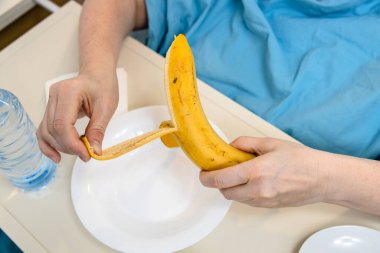 patient peels banana close up in homecare hospital bed at home clipart