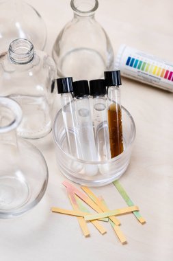 test tubes with various solutions, bottles and used indicators on light desk clipart