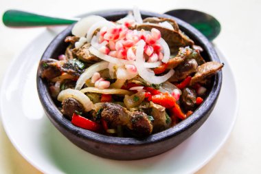 travel to Georgia - portion of Kuchmachi (Georgian dish of livers, hearts and gizzards with sliced fresh onion and pomegranate seeds for topping) in hot ceramic bowl on table close-up in local cafe clipart