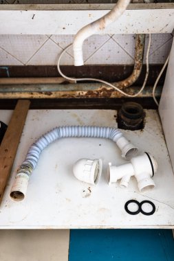 Eski kırsal evlerin mutfağındaki kanalizasyon borusunun yanında kanalizasyon borusu olan eski plastik bir hortum.