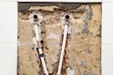 old plumbing with metal-plastic pipes in chiseled brick wall under removed ceramic tiles clipart