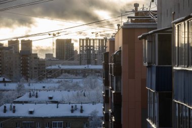 Arka plandaki apartman ve modern yerleşim alanlarının cepheleri kış akşamında güneşin batışıyla aydınlanır.